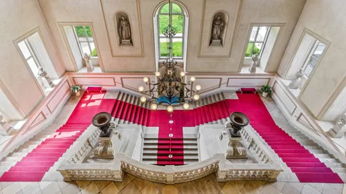 Grand staircase with red carpet, ornate chandelier above.
