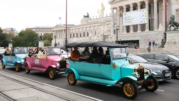 Oldtimer fahren an einem historischen Gebäude vorbei.