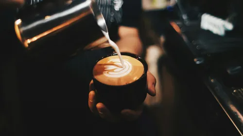 Hand gießt Latte-Art in Kaffeetasse.