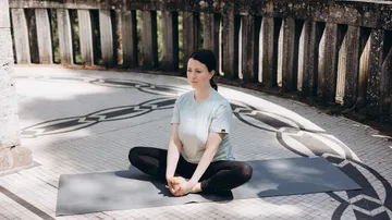 Person meditiert draußen auf Yogamatte.