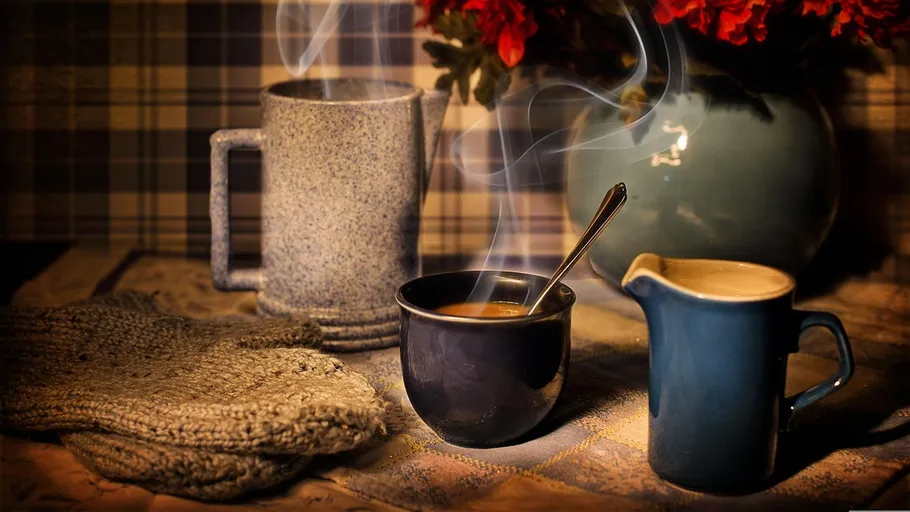 Steamy coffee cup beside vase and pitcher.