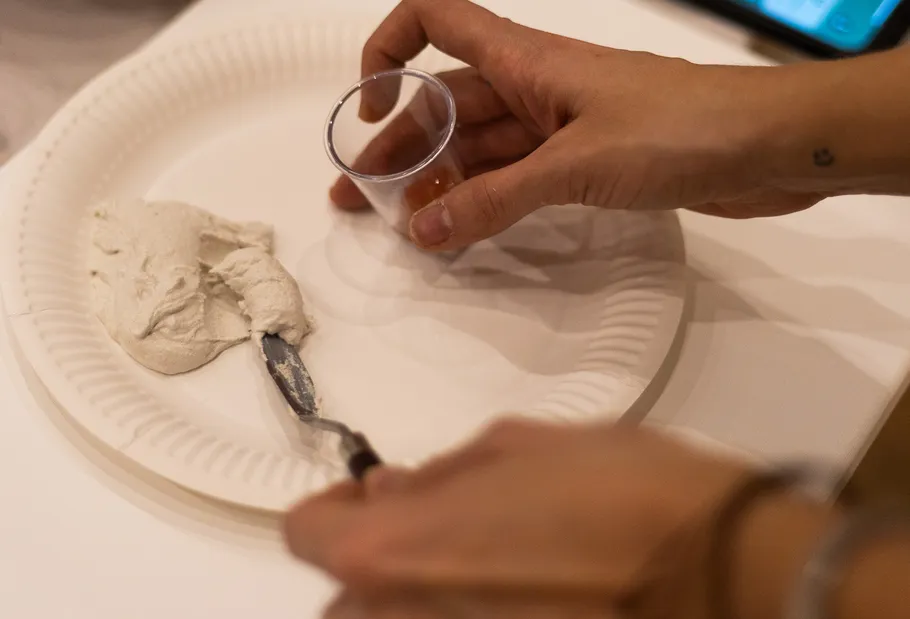 Hand holding cup with spread on paper plate.