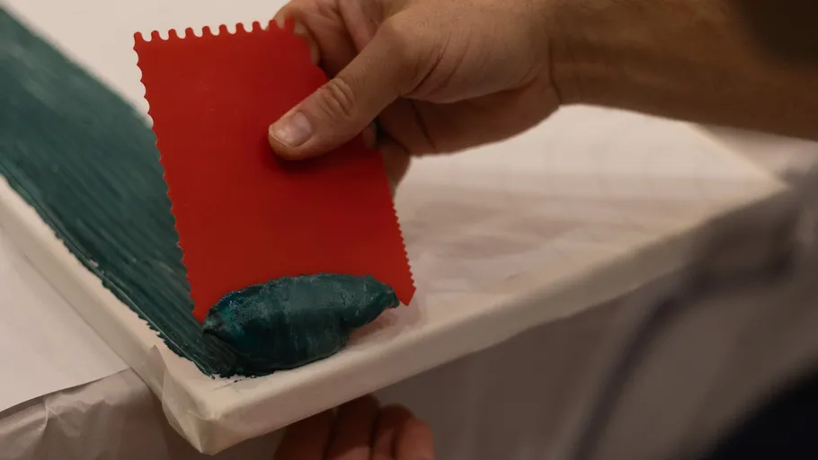 Hand spreads green paste on canvas with scraper.