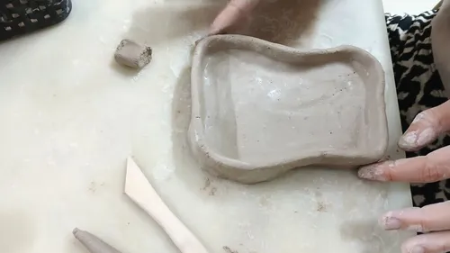 Hände formen Ton zu einem kleinen Tablett.