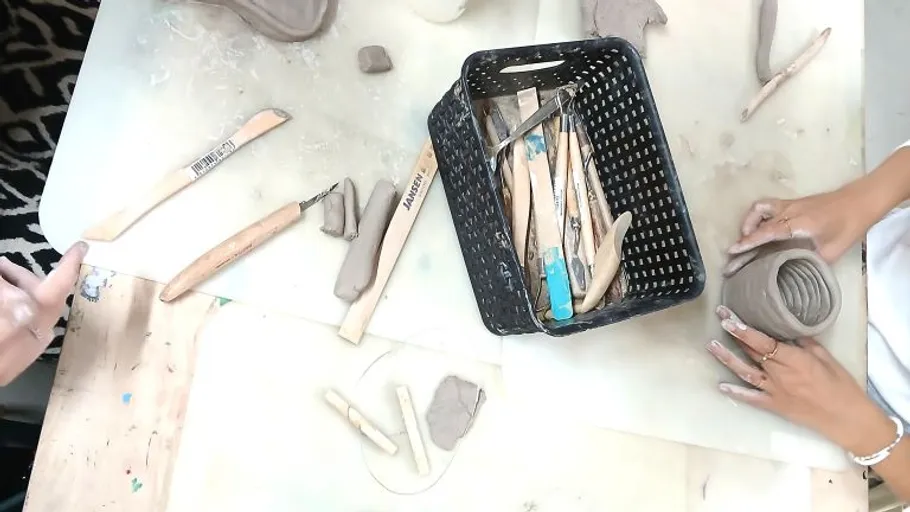 Hände formen Ton mit Töpferwerkzeugen in der Nähe.