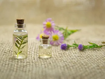 Two bottles of liquid stand on burlap, surrounded by blossoms.