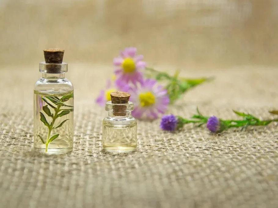 Two bottles of liquid stand on burlap, surrounded by blossoms.