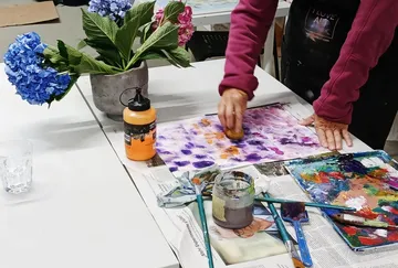 Person painting with sponge on paper, flowers nearby.