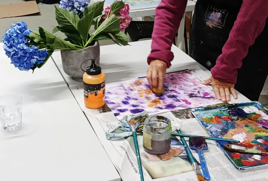 Person malt mit Schwamm auf Papier, Blumen daneben.