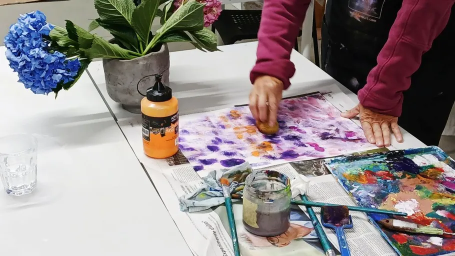 Person malt mit Schwamm auf Papier, Blumen daneben.