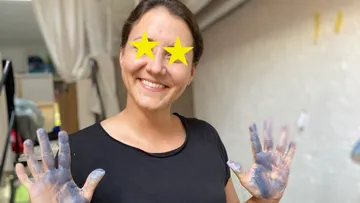 Woman smiling, hands covered in paint, indoors.