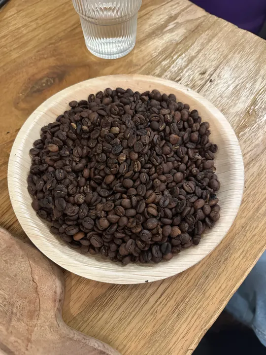 Kaffeebohnen in Schale auf Holzplatte.