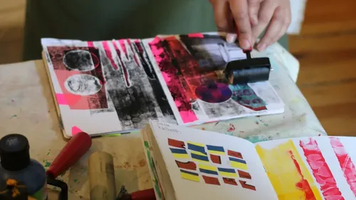 Person benutzt Walze auf buntem Kunstjournal.