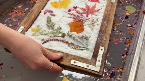 Hand holding wooden frame with pressed flowers.