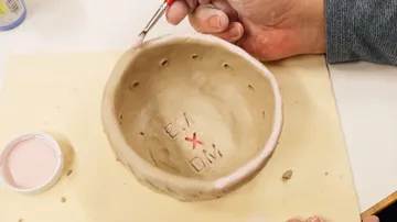 Ton-Schüssel wird auf Holzbrett bemalt.
