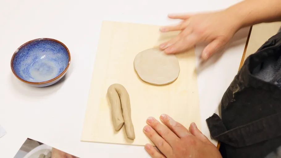 Hands shaping clay on wooden surface.