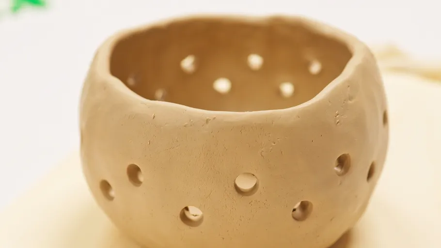 Clay pot with holes on a surface.
