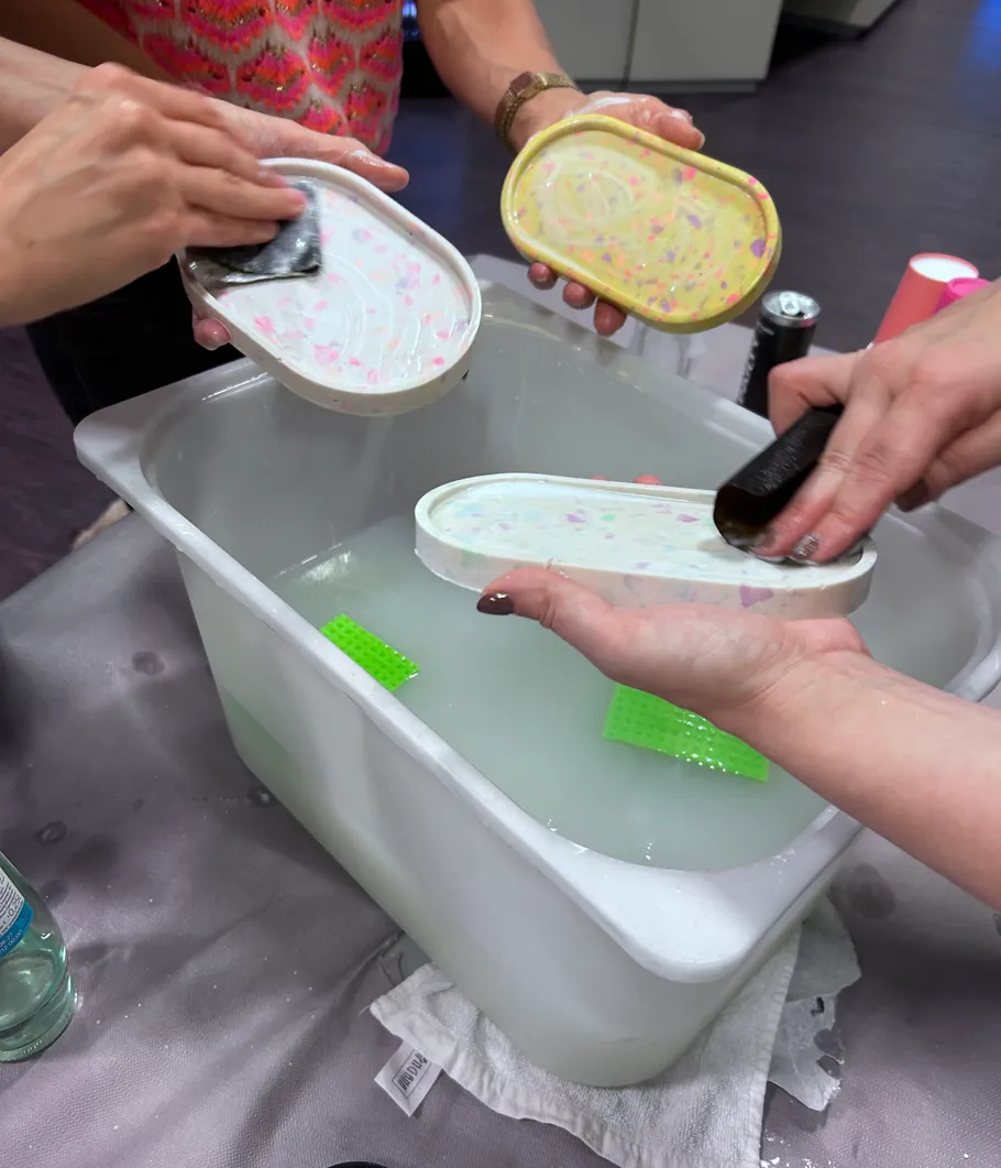 Personen schleifen bunte Seifenschalen über Wasserbehälter.