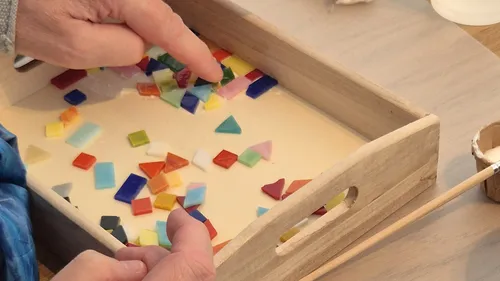 Hands arranging colorful glass pieces in a tray.