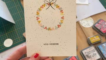 Hand hält Karte mit Herzenkranz-Design.