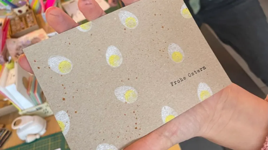 Hand hält Osterkarte mit Eiermuster.