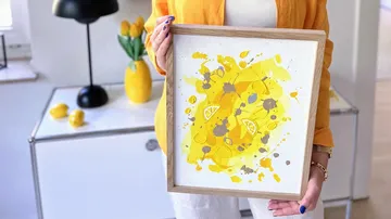 Person holding yellow abstract art in room.