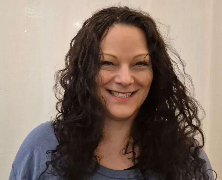 Woman smiling, wearing a blue shirt, indoors.