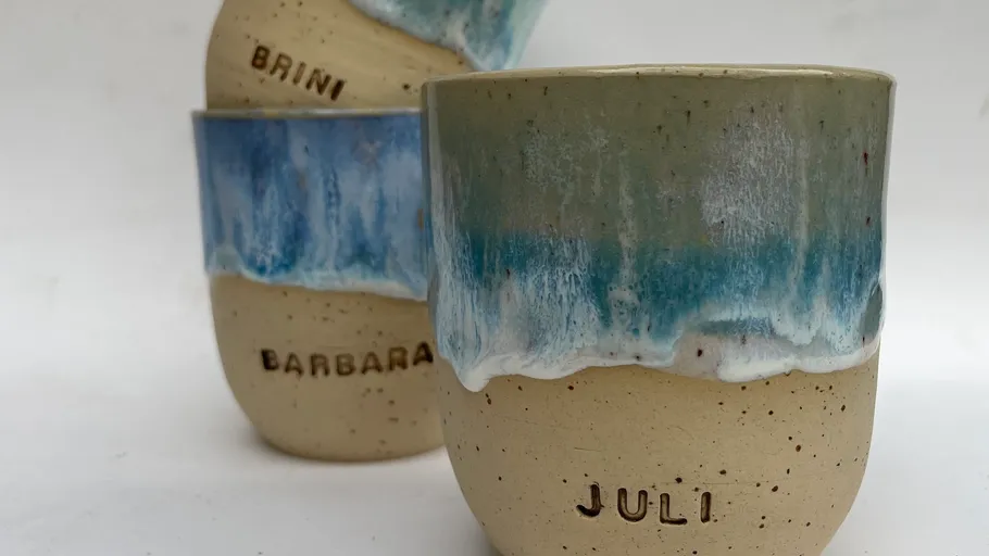 Keramikbecher mit Namen, blaue Glasur, weißer Hintergrund.