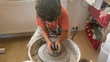 Kind formt Ton an Töpferscheibe drinnen.