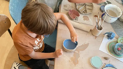 Child painting pottery in art classroom.