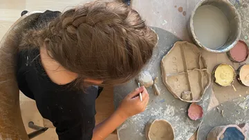 Person formt Tonobjekte an einem Tisch.
