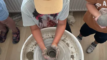 Child making pottery on spinning wheel indoors.