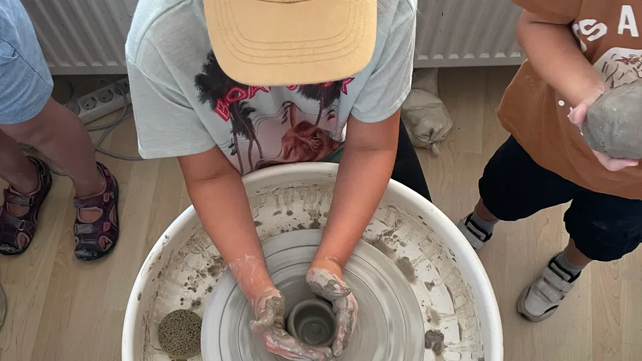 Child making pottery on spinning wheel indoors.