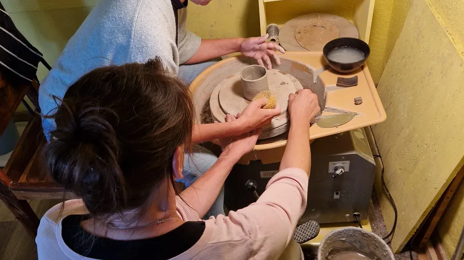 Zwei Personen formen Ton auf Töpferscheibe.