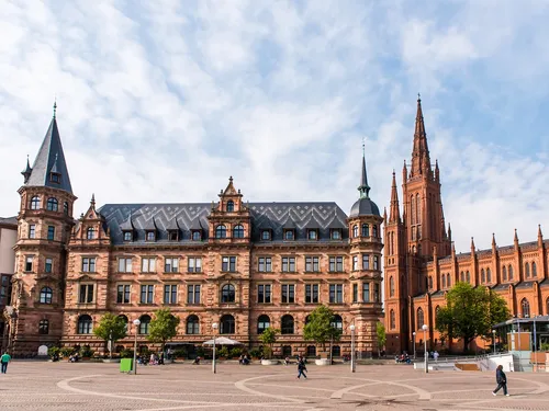 Historic building with towers stands on a square.