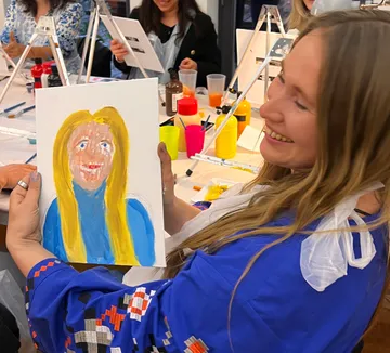 Smiling woman holds colorful portrait painting.