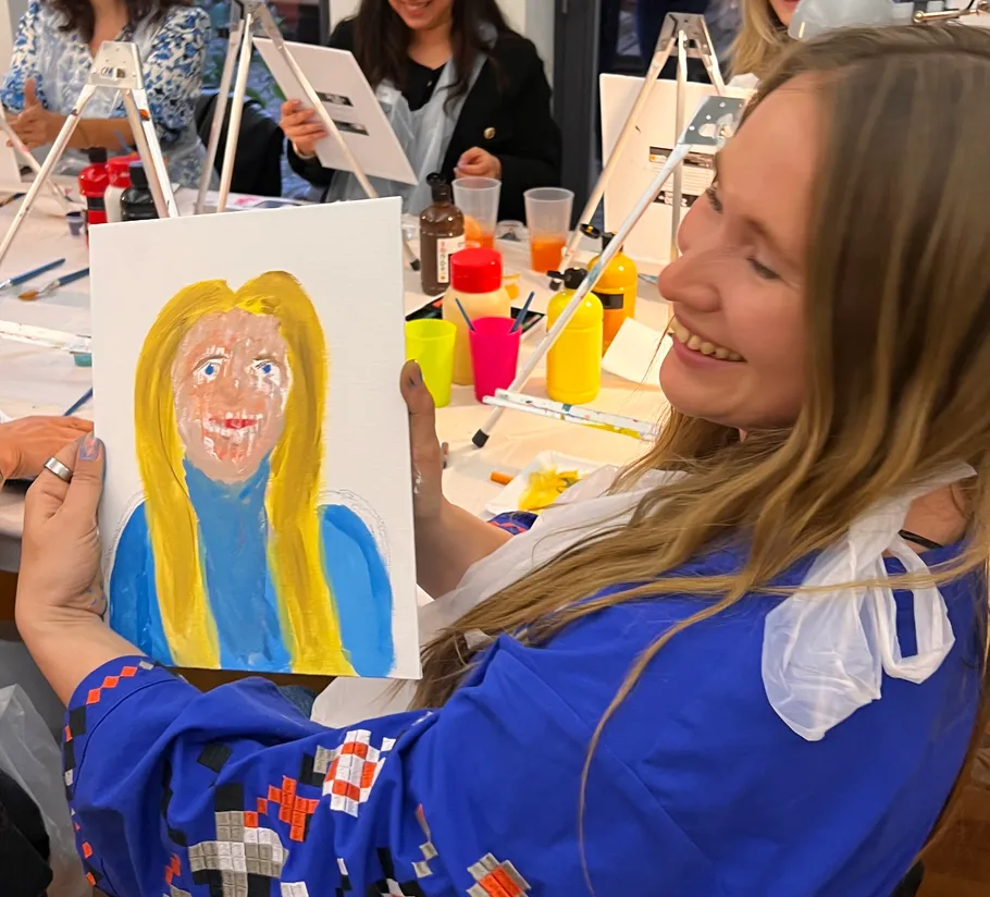 Smiling woman holds colorful portrait painting.