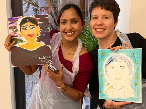 Two people smiling, holding artistic portraits indoors.