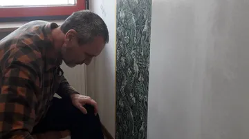 Man inspecting wallpaper in a room.