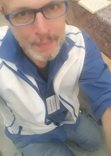 Man with glasses wearing blue jacket indoors.