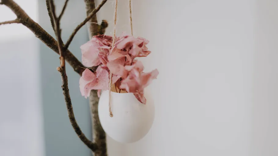 Eggshell hanging on branch with pink flowers.
