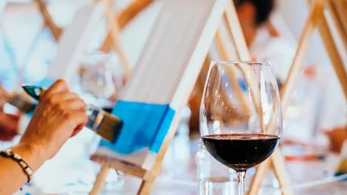 Person painting canvas with glass of wine.