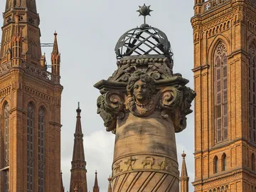 Säule mit weiblicher Statue, umgeben von hohen Gebäuden.