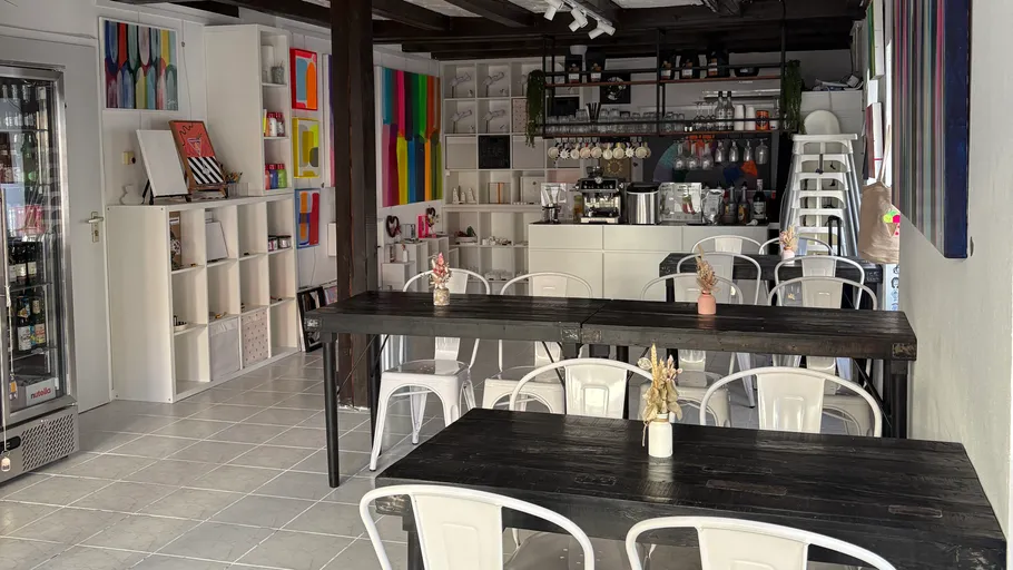 Kleines Café mit Tischen und bunten Gemälden.