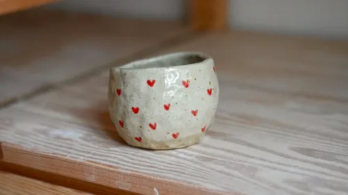 Keramikbecher mit roten Herzen auf Holzoberfläche.