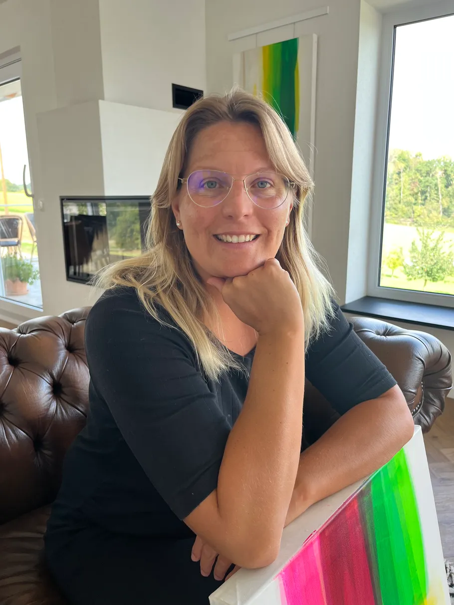 Woman sitting indoors with colorful painting.