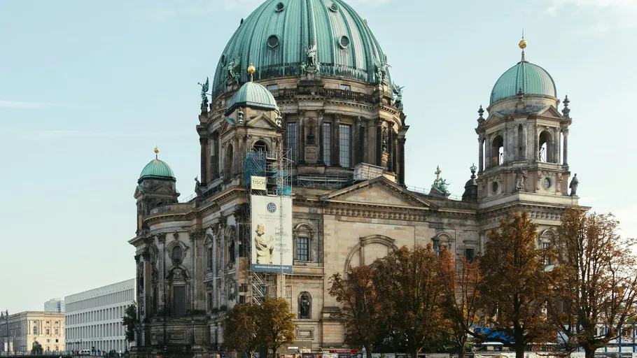 Large historic cathedral with green domes, trees surrounding.
