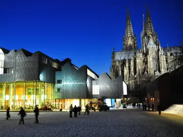 Modern buildings stand next to a Gothic cathedral at night.