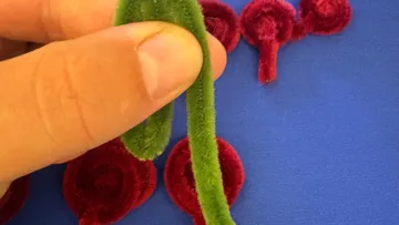 Hand holding green chenille stem, red decorations nearby.
