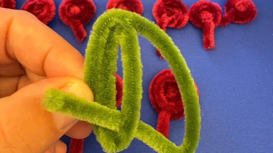 Hand holding green pipe cleaner loop, red spirals behind.